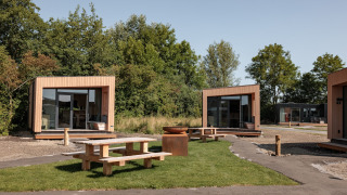 Moderne houten tiny houses bij Noordzee Résidence De Banjaard met picknicktafels op het grasveld.