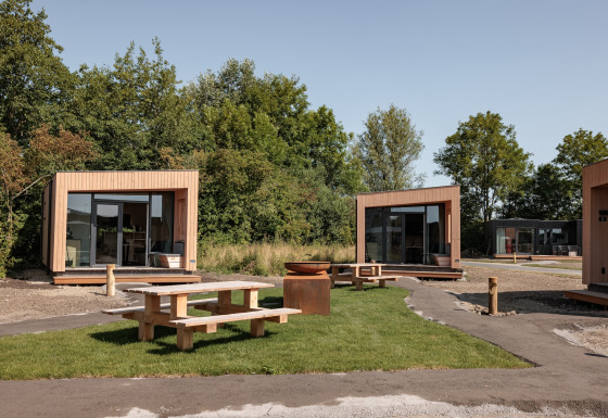 Contemporary wooden tiny houses at Noordzee Résidence De Banjaard with picnic tables on green lawn.