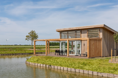 Moderne houten lodge aan het water in Water Village 4, met een terras, buitentafel en groene omgeving.