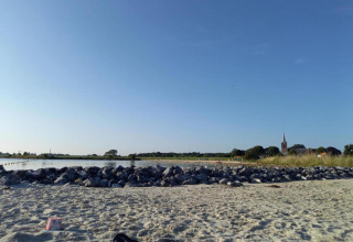 Strandbillede fra Park Wijdenes 3 i Holland med sand, sten, hav og kirketårn i baggrunden.