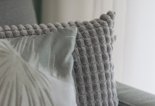 Detalje af grå pyntepuder på en sofa på Park Wijdenes 3-lodge i Holland, moderne og hyggelig stemning.