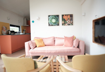 Lyst opholdsområde med lyserød sofa, køkken i baggrunden og grøntsagsbilleder på væggen, Resort «Callantsoog 2».