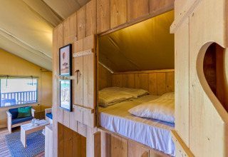 Cozy interior of a safari tent lodge with wooden beds, lounge area, and decor at IJsselhof, Netherlands.