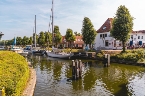 Sailboats docked on a canal by white buildings and green trees at Villa Holiday Park IJsselhof, Netherlands.