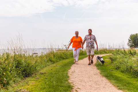 Couple walking their dog by the water at Villa Holiday Park IJsselhof 12, Netherlands, on a cloudy day.