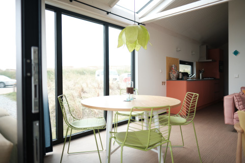 Lichte eetruimte met groene stoelen, ronde tafel, grote ramen en moderne keuken in Resort Callantsoog 2.
