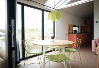 Lichte eetruimte met groene stoelen, ronde tafel, grote ramen en moderne keuken in Resort Callantsoog 2.