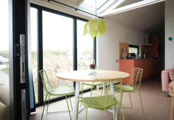 Lys spisestue med grønne stole og bord, store vinduer, og moderne køkken i Resort Callantsoog 2.