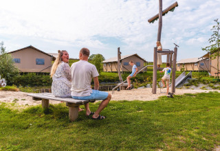 Familie genießt Zeit auf Spielplatz vor Safarizelten im Villa Holiday Park IJsselhof, Niederlande.