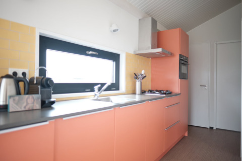 Moderne keuken in Resort Callantsoog 2 in Nederland met oranje keukenkasten, fornuis en oven.
