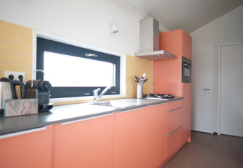 Moderne køkken i Resort Callantsoog 2 i Holland med orange skabe, gaskomfur og kaffemaskine.