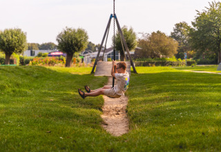 Boy swinging on a chain swing at Villa Holiday Park IJsselhof 12, surrounded by lush grass in the Netherlands.