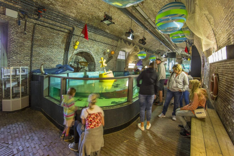 Visitors explore an indoor aquarium housed in a brick-walled lodge, featuring colorful aquatic decorations.