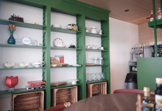 Sfeervolle lodge met groene rekken gevuld met servies, decoratie, spellen en een koffiezetapparaat.