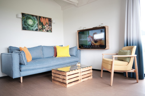 Modern lodge living room at Resort Callantsoog 1, Netherlands, with blue sofa, yellow chair and wall TV.