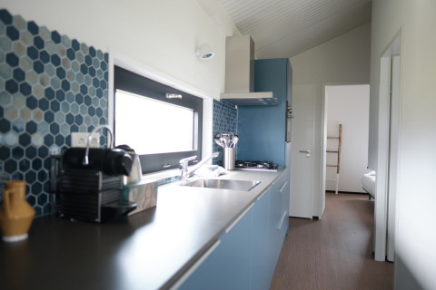 Modern kitchen with blue cabinets, hexagonal tiles, and bedroom view in Resort Callantsoog 1, Netherlands.
