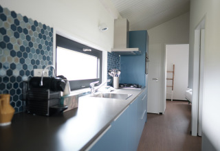 Modern kitchen with blue cabinets, hexagonal tiles, and bedroom view in Resort Callantsoog 1, Netherlands.
