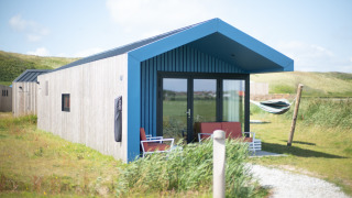 Moderne lodge bij Resort Callantsoog 1 met blauw dak, terras en hangmat tussen de groene duinen.