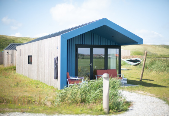 Modern lodge at Resort Callantsoog 1 with blue roof, patio seating, and hammock in grassy dunes setting.