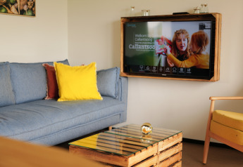 Sala del Resort Callantsoog 1 con sofá azul, cojín amarillo, TV en la pared y mesa de cristal en Países Bajos.