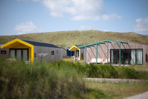 Modern cabins with yellow roofs set by grassy dunes under a blue sky, typical for a scenic lodge setting.
