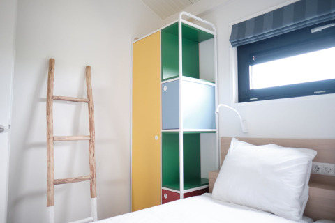 Bright bedroom at Resort Callantsoog 1 in the Netherlands with colorful cabinet, ladder, and window.