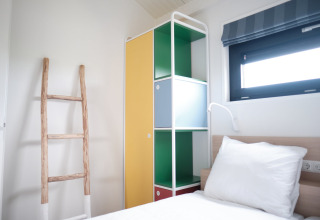 Bright bedroom at Resort Callantsoog 1 in the Netherlands with colorful cabinet, ladder, and window.