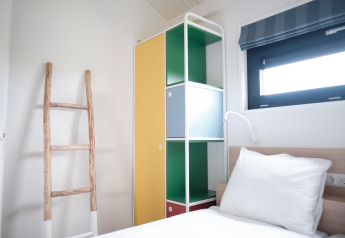 Dormitorio luminoso en Resort Callantsoog 1 en los Países Bajos con armario colorido, escalera y ventana.