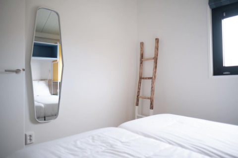 Bright room at Resort Callantsoog 1 in the Netherlands with bed, mirror, window, and decorative ladder.