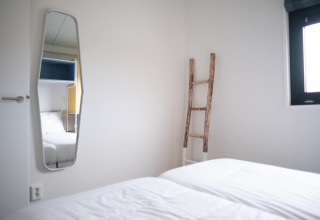 Bright room at Resort Callantsoog 1 in the Netherlands with bed, mirror, window, and decorative ladder.