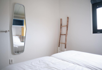 Habitación luminosa en el Resort Callantsoog 1 en los Países Bajos con cama, espejo, ventana y escalera decorativa.