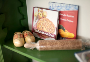 Hylde med hollandske kogebøger, traditionelle trætøfler og en krydderrulle på et lodgeværelse.