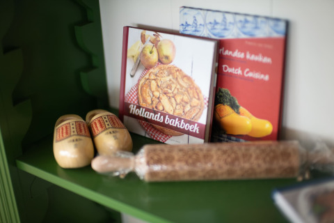 Plank met Nederlandse kookboeken, houten klompen en een speculaasroller in een lodge omgeving.
