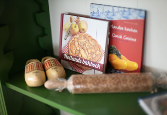 Estante con libros de cocina holandesa, zuecos de madera y un rodillo de especias en un albergue.