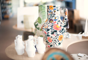 Grande carafe en céramique colorée à motif floral exposée dans un lodge, entourée de petites vases blanches.