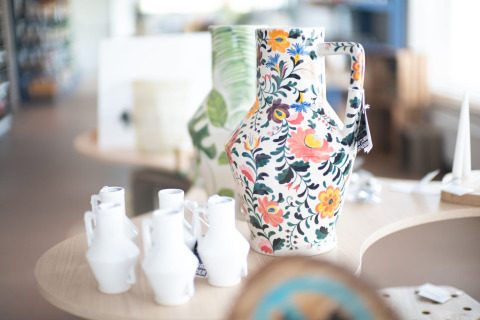 Large, colorful ceramic jug with floral design displayed in a lodge, surrounded by small white vases.