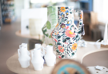 Stort, farverigt keramikkande med blomsterdesign udstillet i en lodge med små hvide vaser omkring.