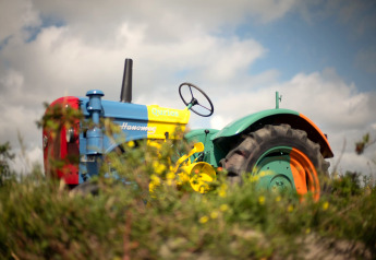 Un tracteur Hanomag coloré photographié dans un lodge, entouré d’herbe et sous un ciel nuageux.