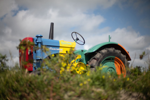 A colorful Hanomag tractor pictured at a lodge, surrounded by grass and a cloudy blue sky overhead.