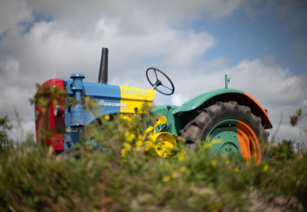 Un colorido tractor Hanomag en una casa rural, rodeado de césped verde y un cielo nublado al fondo.