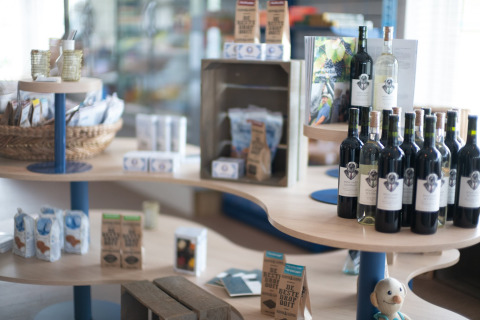 Lodgewinkel met wijnflessen, streekproducten en geschenken uitgestald op gebogen houten rekken.