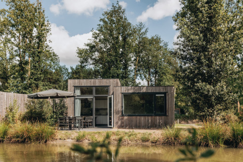 Feriebolig Holiday Park Schaijk 3, et lille moderne træhus ved en sø, omgivet af træer og natur.
