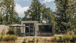 Tiny house Holiday Park Schaijk 3, moderna casetta in legno vicino a uno stagno, immersa nel verde.