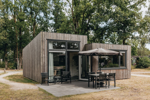 Tiny house moderna in legno con patio e sedute esterne al Holiday Park Schaijk, circondata da alberi.