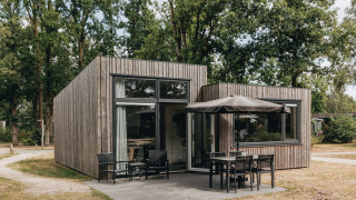 Tiny house moderna in legno con patio e sedute esterne al Holiday Park Schaijk, circondata da alberi.