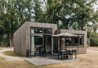 Tiny house moderne en bois avec terrasse et mobilier de jardin au Holiday Park Schaijk, entourée d’arbres.