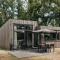 Tiny house moderne en bois avec terrasse et mobilier de jardin au Holiday Park Schaijk, entourée d’arbres.