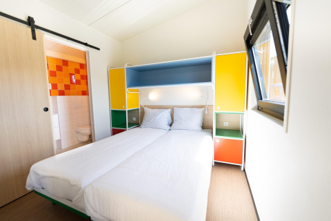 Lichte slaapkamer in Resort Callantsoog 5, Nederland, met tweepersoonsbed, kleurrijke kasten en badkamer.