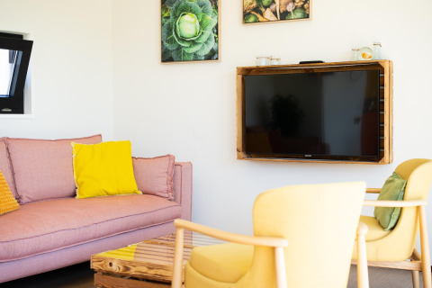 Lichte woonkamer in Resort «Callantsoog 5» met pastelkleurige zitbank, tv en gele tinten in Nederland.
