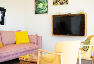 Lichte woonkamer in Resort «Callantsoog 5» met pastelkleurige zitbank, tv en gele tinten in Nederland.